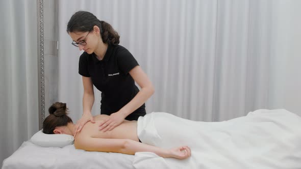 Female therapist massages a young woman on her back and shoulders. Relaxing massage.