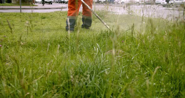 Worker in Orange Overalls Mows the Grass on the Lawn with a Gasoline Mower, Slow Motion Front View alt