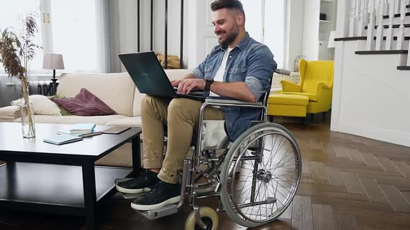 Bearded Man in Wheelchair Remotely Working on Personal Computer at Home alt