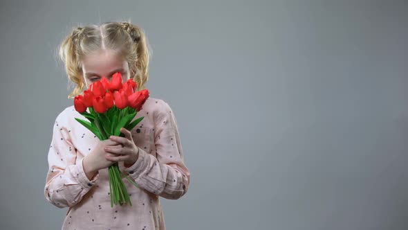 Adorable Girl Smelling Flowers and Smiling on Grey Background, Holiday Mood alt