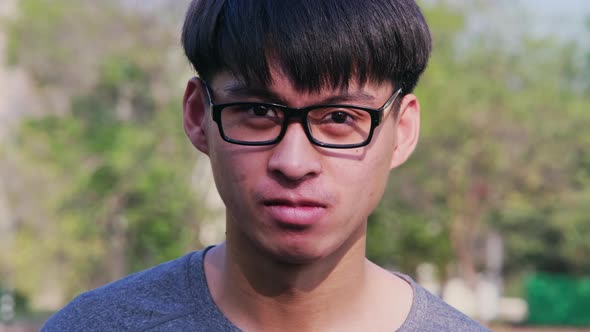Portrait of a confident young man in glasses and casual gray t-shirt standing in a summer garden. alt