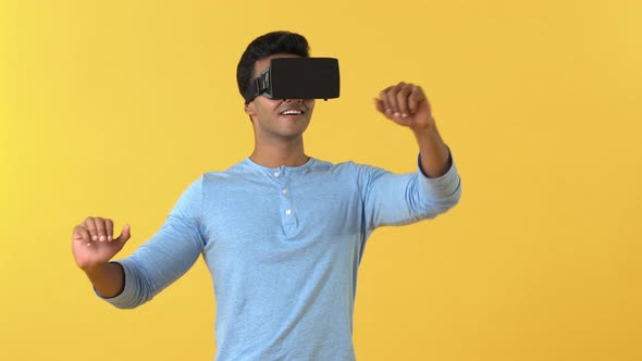 Fun Indian man getting in the media in VR gadgets isolated on yellow background