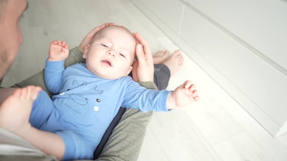 Father Plays with a Smiling Baby Son Lying on Knees at Home Together