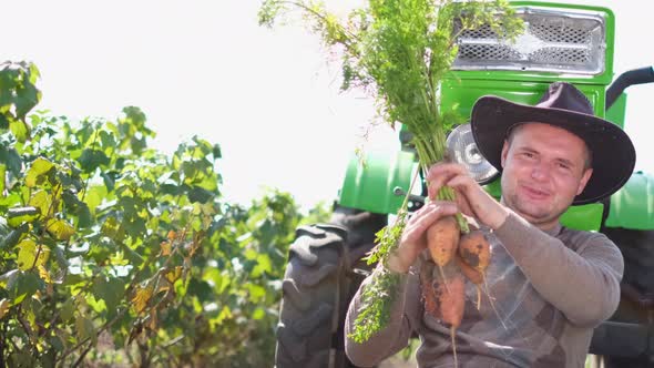 Happy Farmer with Carrot in a Field Near His Tractor alt