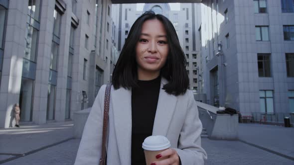 Portrait of a Young Adult Asian Businesswoman Walking From Office with a Coffee Cup in Slow Motion alt