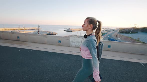 Young Female in Sportswear Walk Along Harbor at Coastal City alt