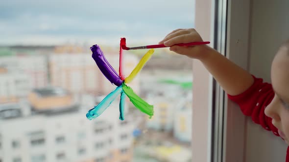 Child draw snowflake in rainbow colours on window with paints. Caucasian female person decorate room alt