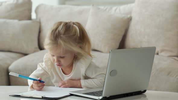 Little Girl Using a Laptop Computer Studying Through an Online Elearning System While Sitting in the alt