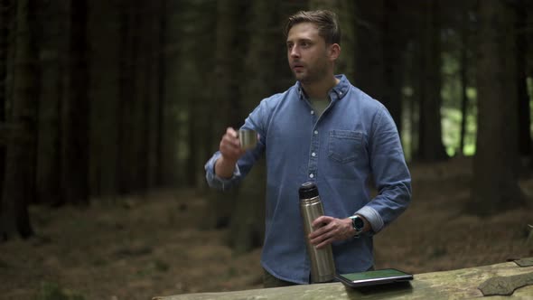 Hiker drinking from thermos flask in the forest alt