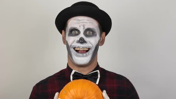 A Terrible Man in Clown Makeup and with a Pumpkin on His Head Grimaces and Waves His Hand in