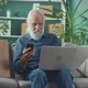 A Concentrated Older Man is Holding a Phone While Looking Excitedly at a Laptop - VideoHive Item for Sale