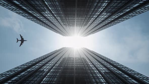 Airplane flies between high rise buildings crossing sun flare and reflects on glass facades. alt