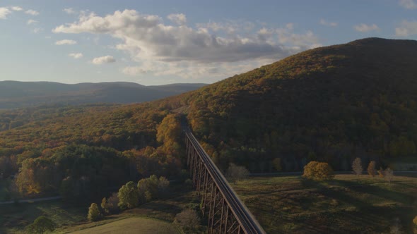 Aerial of sunlight falling on green valley landscape and railroad bridge alt