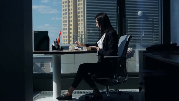 Business Woman Eats at the Workplace in a Modern Beautiful Office Near the Panoramic Window and