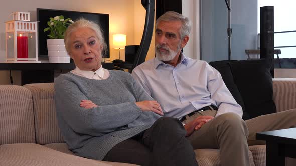 An Elderly Couple Sits on A Couch in An Apartment and Talks to The Camera alt