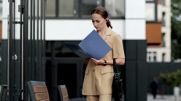 Beautiful professional businesswoman taking out documents from her bag near the office alt