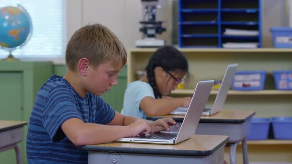 Students in school classroom working on laptop computers alt