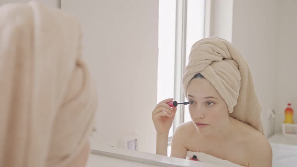 Teenage girl applying makeup in front of the bathroom mirror alt