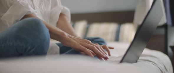 Woman hands typing something on a laptop keyboard in the bedroom. alt