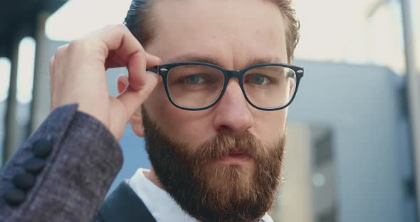 Office Manager which Correcting His Glasses while Looking at Camera Outdoors Near Office Building  alt