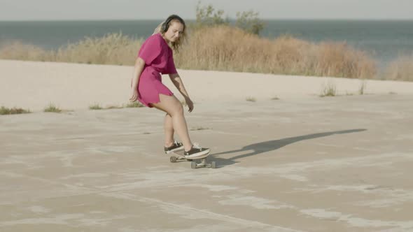 Cheerful Girl with Headphones Riding Skateboard Near Ocean alt