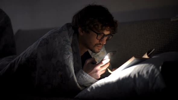 Man Reads a Book with a Flashlight Under the Covers at Night