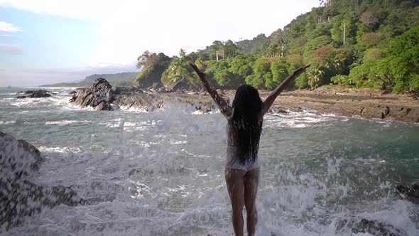 Ocean waves splashing against rocks with woman standing on shore alt