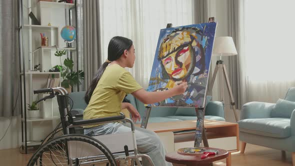 Side View Of Asian Artist Girl In Wheelchair Holding Paintbrush Mixed Colour Thinking And Painting alt