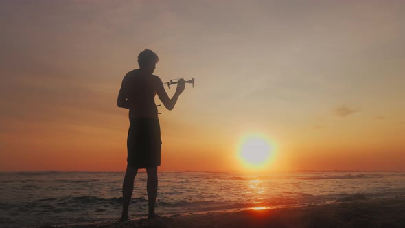 The Silhouette of a Man in Shorts Against the Background of the Ocean and the Sunset Sky Launches a