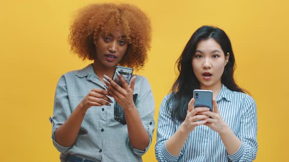 Two Young Women Checking Social Networks and Showing Their Surprise with Wierd Face Expression alt