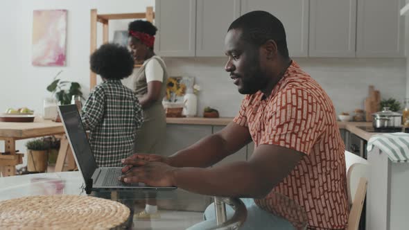 African-American Man Working on Laptop in Kitchen alt