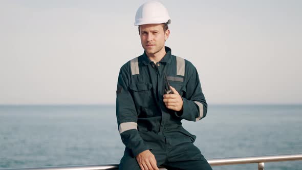 Young Port Worker in Helmet and Coverall Using Vhf Radio Controlling Work Process in Shipping Port alt