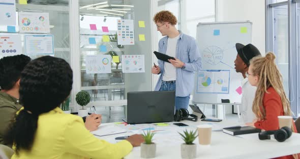 Guy with Standing Near Glass Wall with Diagramms and Explaining to His Colleagues alt