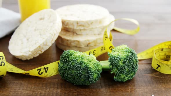 Broccoli, granola bar, yellow cherries and measurement tape on wooden table alt