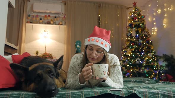 Pretty Woman in a Warm Knitted Sweater Drinks Hot Chocolate and Relaxes While Lying on the Bed with
