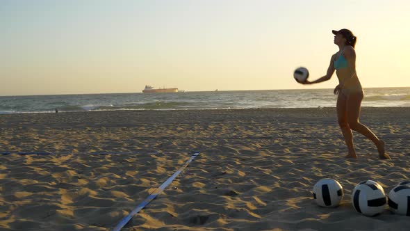 Women players play beach volleyball and a player jump serves serving the ball. alt