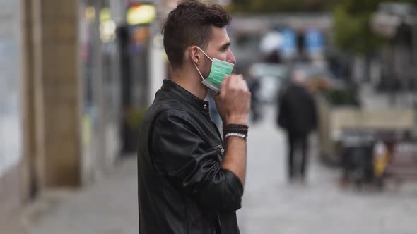 A young man in a leatherette jacket with a modern hairstyle on a busy street, putting on a green pro alt