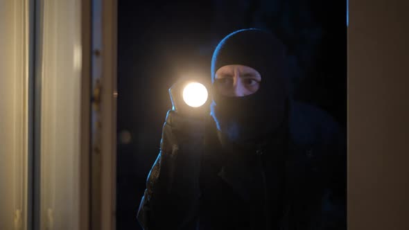 Male Thief Lighting with Flashlight at Night Standing Behind Glass Window alt