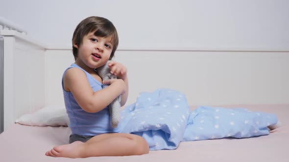 Child Is Sitting on the Bed in a T-shirt and Playing alt