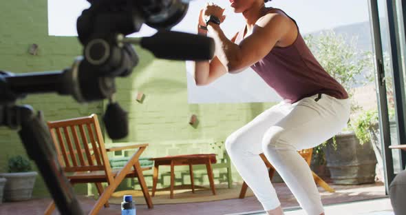 Fit african american man exercising at home, doing squats and filming fitness vlog alt