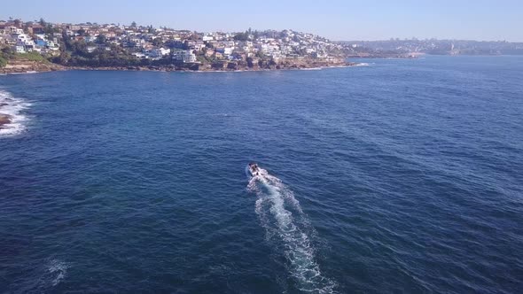 Aerial fly over drone following a speed fishing boat at the Sydney coastal beach seaside alt