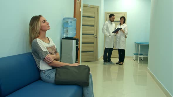 Female Patient Waiting in Hospital Hall While Two Doctors Consulting alt