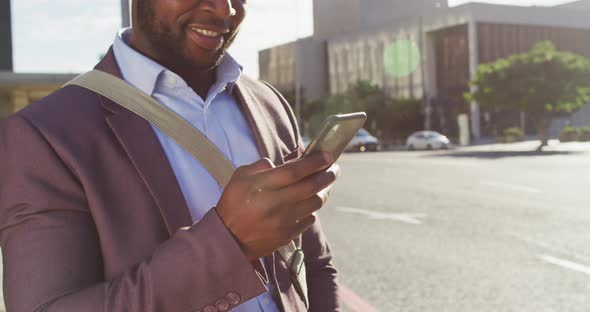 Midsection of african american man in city, standing in the sun using smartphone alt
