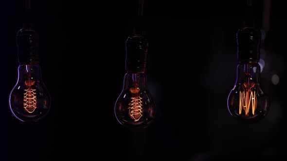 Three vintage decorative light bulbs hang in the dark and glow on a blurred background.
