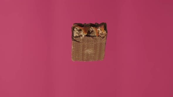 A Delicious and Unhealthy Chocolate Bar Rotates on a Pink Background. Bitten Sweets Isolated. The alt