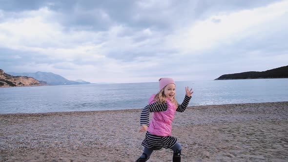 Cute little girl in pink hat runs along the beach along the sea in spring time. Freedom concept alt