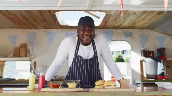Portrait of african american man wearing apron smiling while standing in the food truck alt