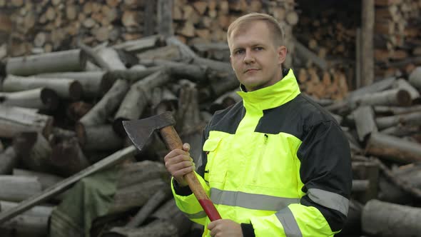 Man Woodcutter Lumberjack with Small Axe. Sawn Logs, Firewood Background. Asks To Follow Him alt