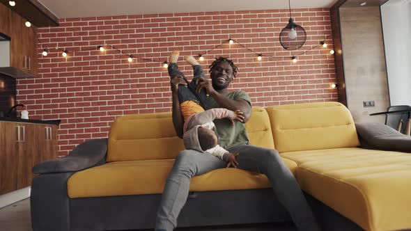 African Father Playing with Little Adorable Child Son Having Fun on Sofa alt