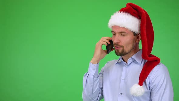 A Young Handsome Man in a Christmas Hat Talks on a Smartphone with a Smile - Green Screen Studio alt